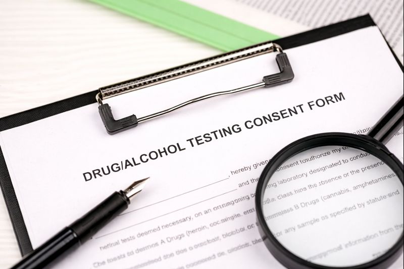Drug and alcohol testing consent form on clipboard with pen and magnifying glass